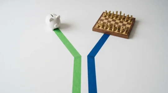 Deux chemins tracés sur une table blanche : un ruban vert vers une tirelire, un ruban bleu vers un échiquier, symbolisant le choix entre épargne et crédit.
